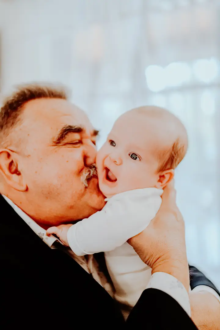Dziadek całuje wnuka w dniu Chrztu Świętego – fotografia rodzinna