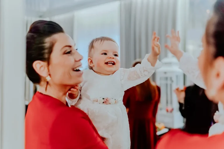 Uśmiechnięte dziecko w białej sukience podczas chrztu z mamą/chrzestną