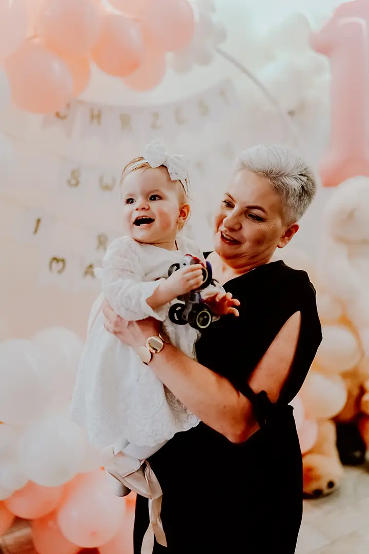 Przyjęcie chrzcielne – dziecko w białej sukience na tle dekoracji z balonów