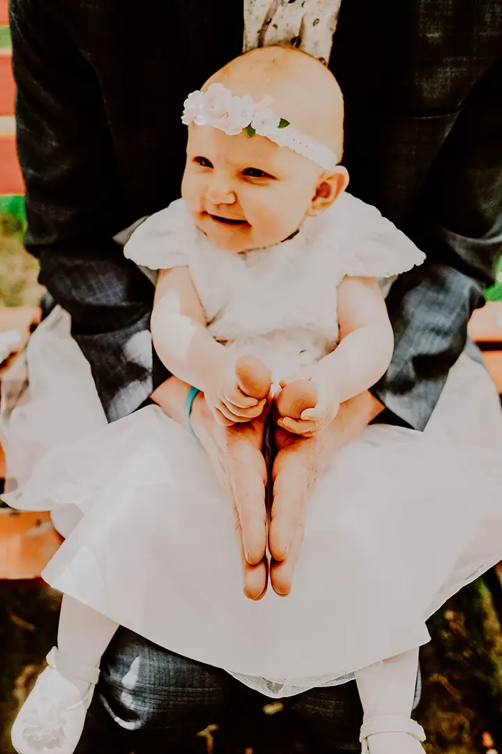 Uśmiechnięte dziecko w białej sukience podczas chrztu, fotografia rodzinna Łódź