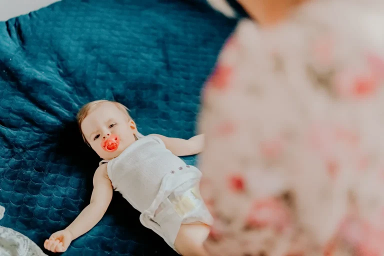 Niemowlę z czerwonym smoczkiem podczas przygotowań do Chrztu Świętego – fotografia domowa